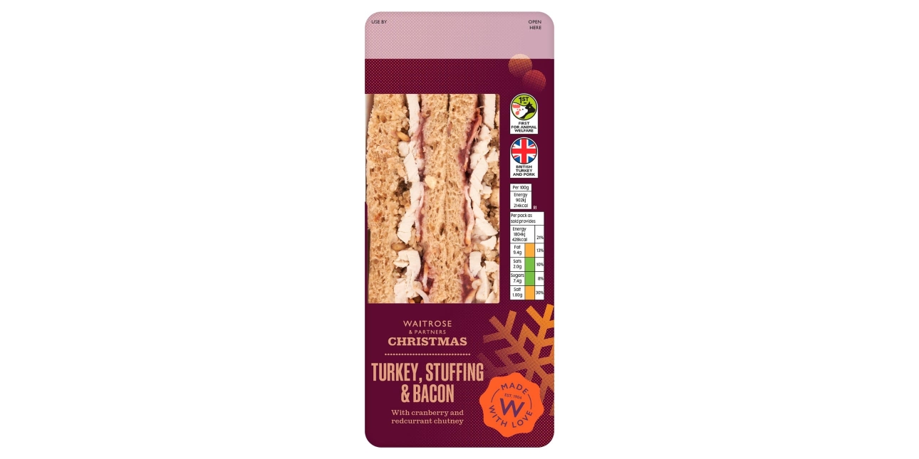A Waitrose Christmas Turkey, Stuffing and Bacon sandwich in a dark red pack with the sandwich visible through a clear window